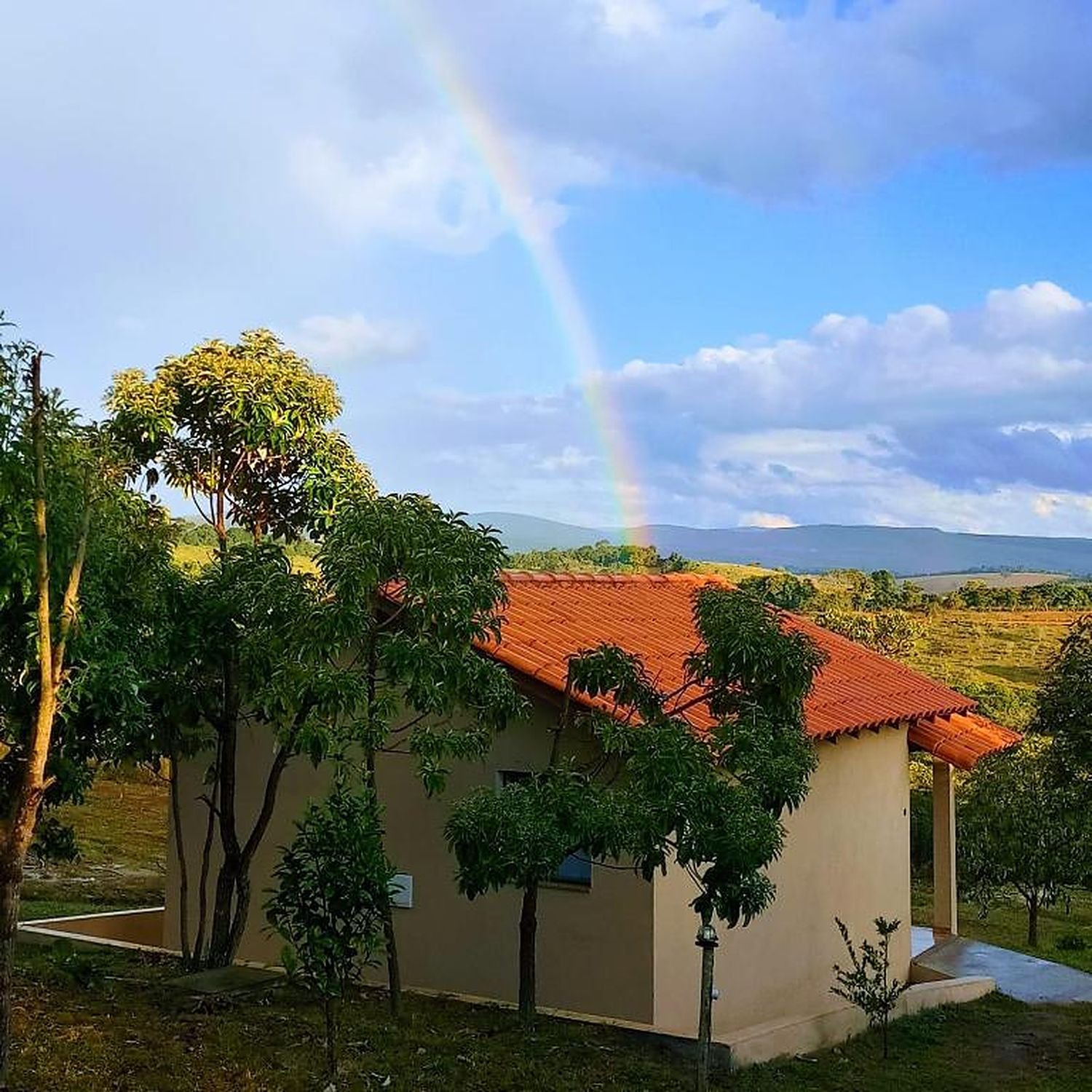 Arco-íris sobre um chalé, com a serra ao fundo